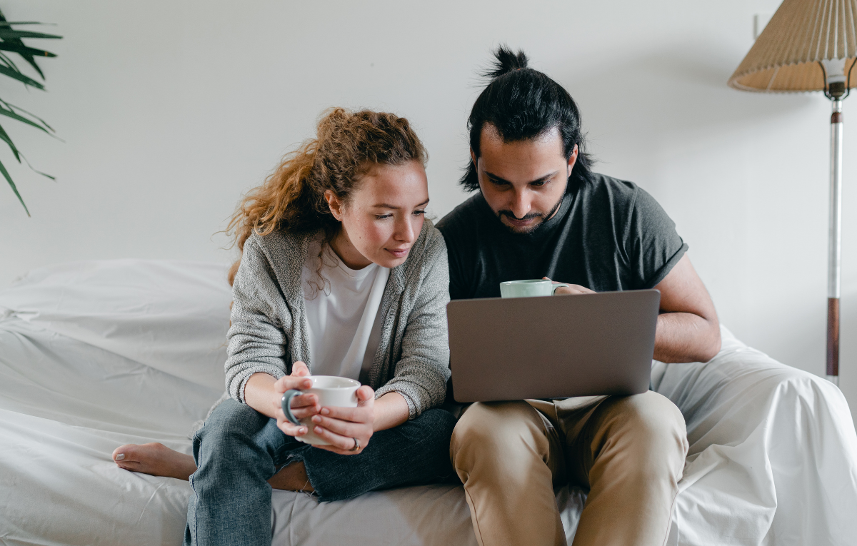 Een vrouw en een man zitten op de bank en kijken samen naar een laptop.